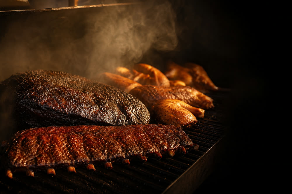 Several cuts of meat smoking together on the grate of a barbecue smoker
